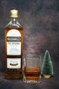 A bottle of Bushmills whiskey, a glass of whiskey and a small new Christmas tree on a dark vintage background