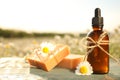 Bottle of chamomile essential oil and soap bars on wooden table in field Royalty Free Stock Photo