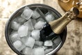 Bottle of champagne in bucket with cubes ice on table. Royalty Free Stock Photo