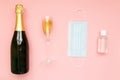 Bottle of champagne face mask hand sanitizing gel and glasses with gold glitter on pink background. Party decor. Christmas,