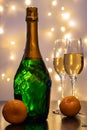 A bottle of champagne, in the foreground, champagne glasses and tangerines.