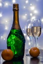 A bottle of champagne, in the foreground, champagne glasses and tangerines, shot in a cold key.