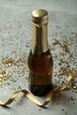 Bottle of champagne, glitter and ribbon on gray texture background
