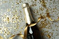 Bottle of champagne, glitter and ribbon on gray texture background