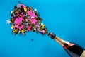 Bottle of champagne with splash of sparkling iridescent confetti on blue screen background. Mock up from pink, gold and Royalty Free Stock Photo