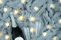 A bottle of champagne and two glasses against the background of gray fur plaid with a luminous garland Royalty Free Stock Photo