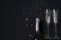 A bottle of champagne and two glasses, golden confetti on a festive black background. Festive concept. Copy space Royalty Free Stock Photo