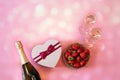 Bottle of champagne, two glasses of champagne, heart shape gft box and fresh strawberry on pink background Royalty Free Stock Photo