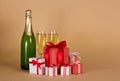 Bottle of champagne, two glasses, lot of Christmas gifts in colorful boxes on beige Royalty Free Stock Photo