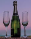 A bottle of champagne with two flute glasses beside it against a beautiful sunset sky Royalty Free Stock Photo