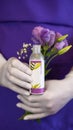 A bottle of cosmetic product in the hands. Lilac flowers.