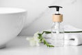 Bottle with dispenser cap, towel and beautiful flower on white table in bathroom, closeup Royalty Free Stock Photo