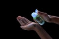 Bottle of essential oil in hand on black dark background. Hands pouring hand sanitizer in transparent bottle. Alcohol gel