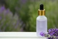Bottle of essential oil and lavender flowers on white wooden table in field, space for text Royalty Free Stock Photo
