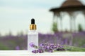 Bottle of essential oil and lavender flowers on white wooden table in field, space for text Royalty Free Stock Photo