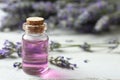 Bottle with essential oil and lavender flowers on wooden table. Space for text