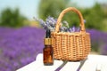 Bottle of essential oil and wicker bag with lavender flowers on white wooden surface outdoors, closeup Royalty Free Stock Photo