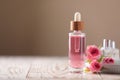 Bottle of essential rose oil and flowers on white wooden table against beige background, space for text Royalty Free Stock Photo