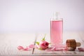 Bottle of essential rose oil and flowers on white wooden table against light background. Space for text Royalty Free Stock Photo