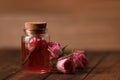 Bottle of essential rose oil and flowers on wooden table, space for text Royalty Free Stock Photo