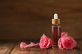 Bottle of essential rose oil and flowers on wooden table, space for text Royalty Free Stock Photo