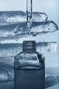 A bottle of face serum and a pipette on the background of pieces of melting ice.