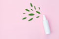 Bottle of facial moisturizing toner or hair spray with and green herbal leaves isolated on pastel pink background, flay layout, t