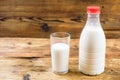 Bottle of fresh farm milk with red lid and glass of milk on wooden background. Side view. Royalty Free Stock Photo