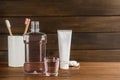 Bottle and glass with mouthwash near other oral hygiene products on wooden table, space for text Royalty Free Stock Photo