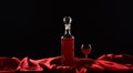 Bottle and glass with red wine on black background with red cloth, satin fabric, silk