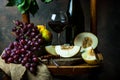 Bottle and glass of red wine, grape and cork on chair. Melon, piece of melon. Pink grape, pear. Still life of food. Dark