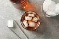 Bottle, glasses with ice cubes and whiskey on grey background