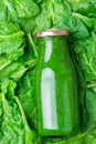 Bottle with Green Fresh Raw Smoothie from Leafy Greens Vegetables Fruits Apples Bananas Kiwi Zucchini on Spinach Leaves Background Royalty Free Stock Photo