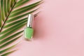 Bottle of green nail polish and palm tree branch on pastel pink background. Manicure and pedicure concept. Flat lay, top view,