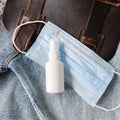 Bottle of hand sanitizer, antimicrobial liquid spray, medical protective mask and brown bag on blue denim background.