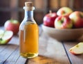 A bottle of homemade apple cider vinegar. Juicy apples and a wooden table in the back.