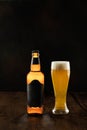 A bottle of light beer with a glass of foamy beer on a wooden table against a dark background Royalty Free Stock Photo