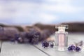 Bottle of luxury perfume and lavender flowers on white wooden table outdoors