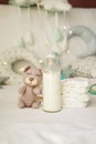 Bottle of milk with bear toy and stack of diapers on bed