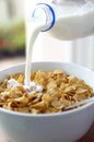 A bottle of milk being poured into a bowl of cereal. Conceptual image shot