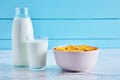 Bottle of milk, bowl of cereal corn flakes and a glass full of milk on a wooden table