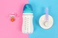 Bottle of milk for newborn baby, pacifier on a pink background and jar with powdered infant formula on blue background