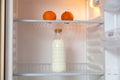 Bottle of milk and oranges stand in empty fridge