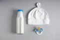 Bottle of milk with pacifier and baby hat on grey background Royalty Free Stock Photo