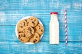 A bottle of milk, a plate of cookies and a paper straw, flat lay.