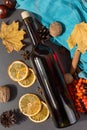 A bottle of mulled wine with spices, a scarf, dry leaves and oranges on a stone table. Autumn mood, a method to keep warm in the