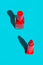 Bottle with nail polish and red crimson lipstick on solid blue background. Bright sunlight strong shadows. Creative minimalist