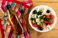 Bottle of oil, fork on napkin, bowl of salad with cucumbers and tomato, black olives, feta cheese on table. Top view Royalty Free Stock Photo