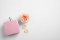 Bottle of perfume, beautiful rose and petals on white background, flat lay