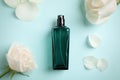 Bottle of perfume, beautiful roses and petals on light blue background, flat lay